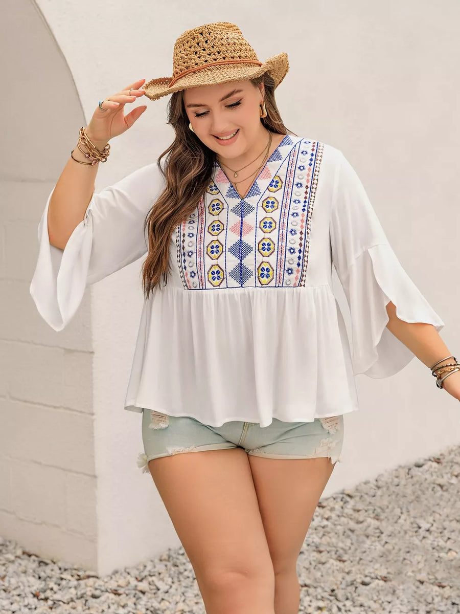 White plus size shirt with vibrant geometric embroidery, bell sleeves, and V-neck.