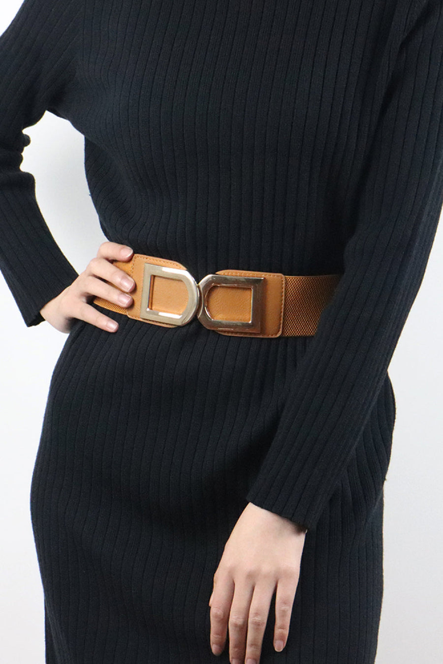 Caramel elastic belt with double gold D-ring buckle cinches a black ribbed dress.