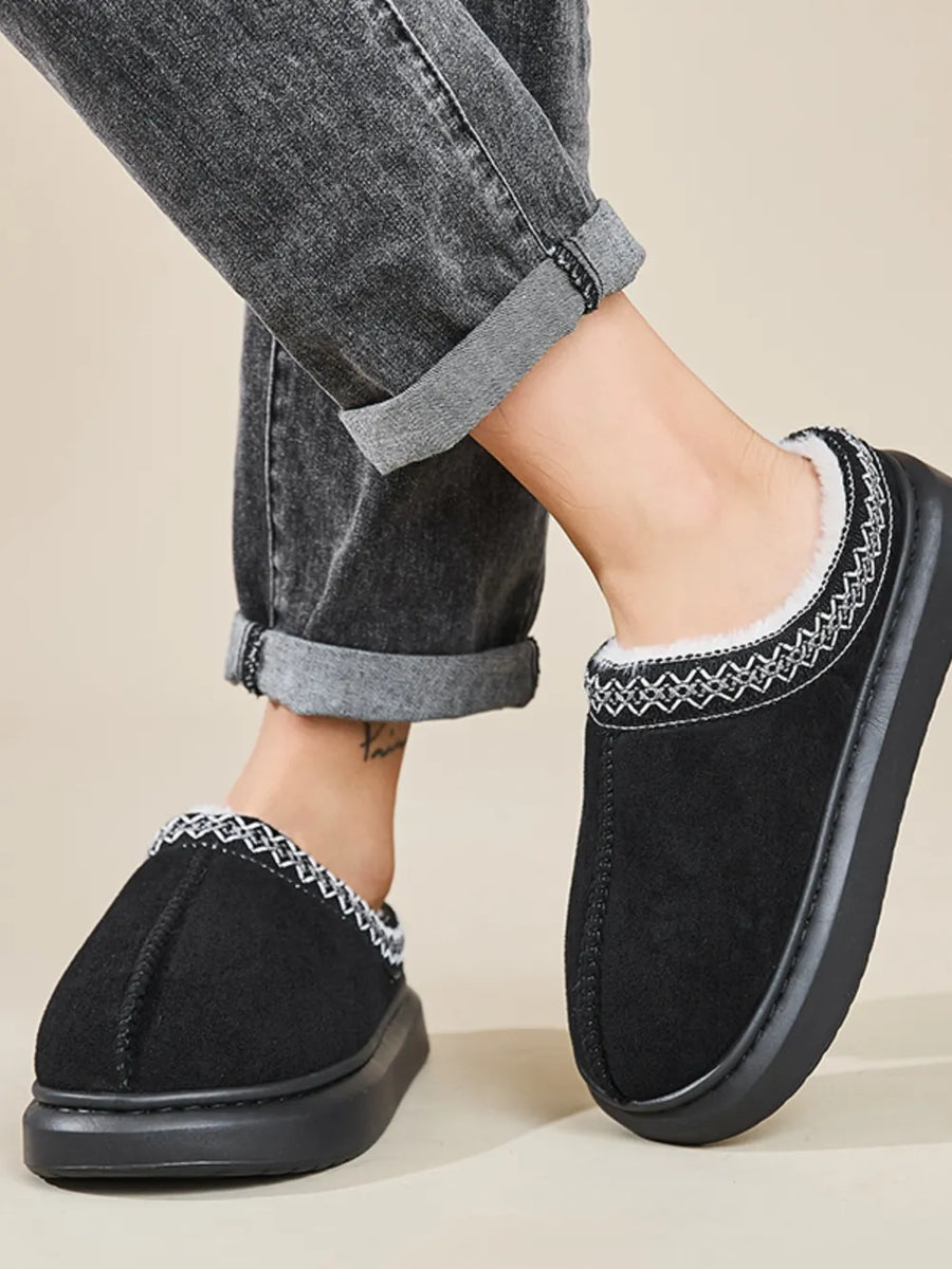 Black shearling house slippers with embroidered trim and thick sole.