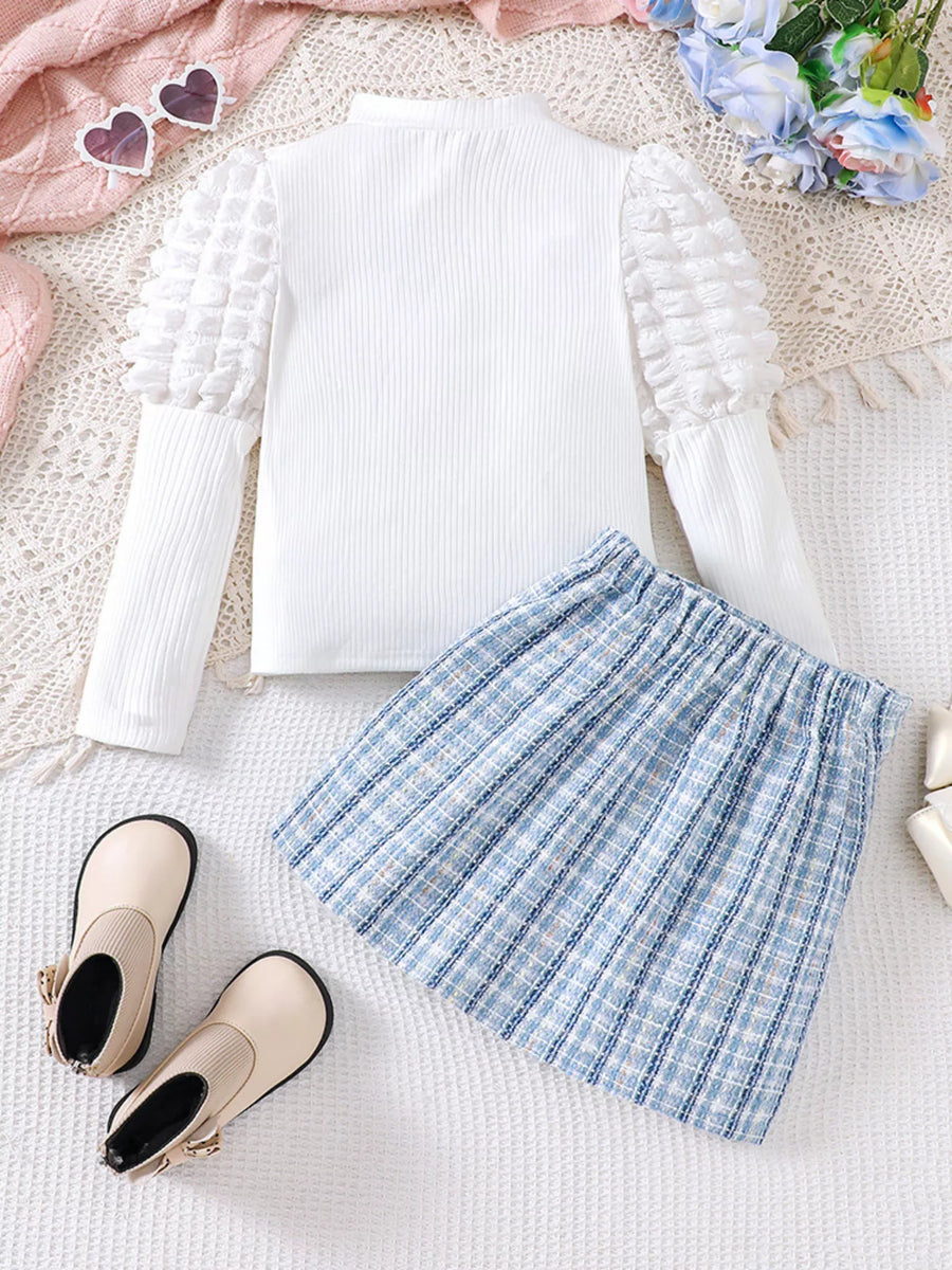 White puff sleeve top with textured sleeves and blue plaid skirt.