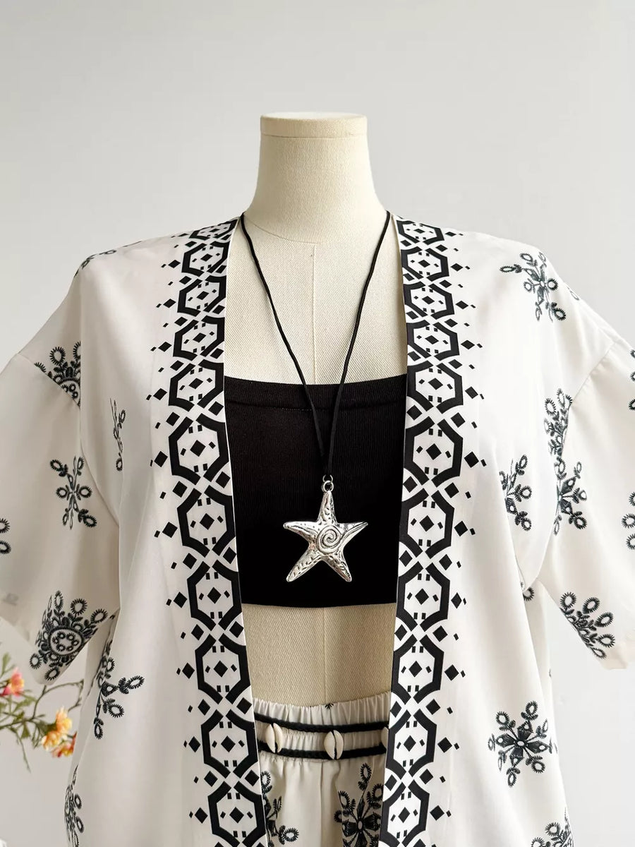 White polyester kimono jacket with black geometric and floral print, worn over a black crop top and shorts.