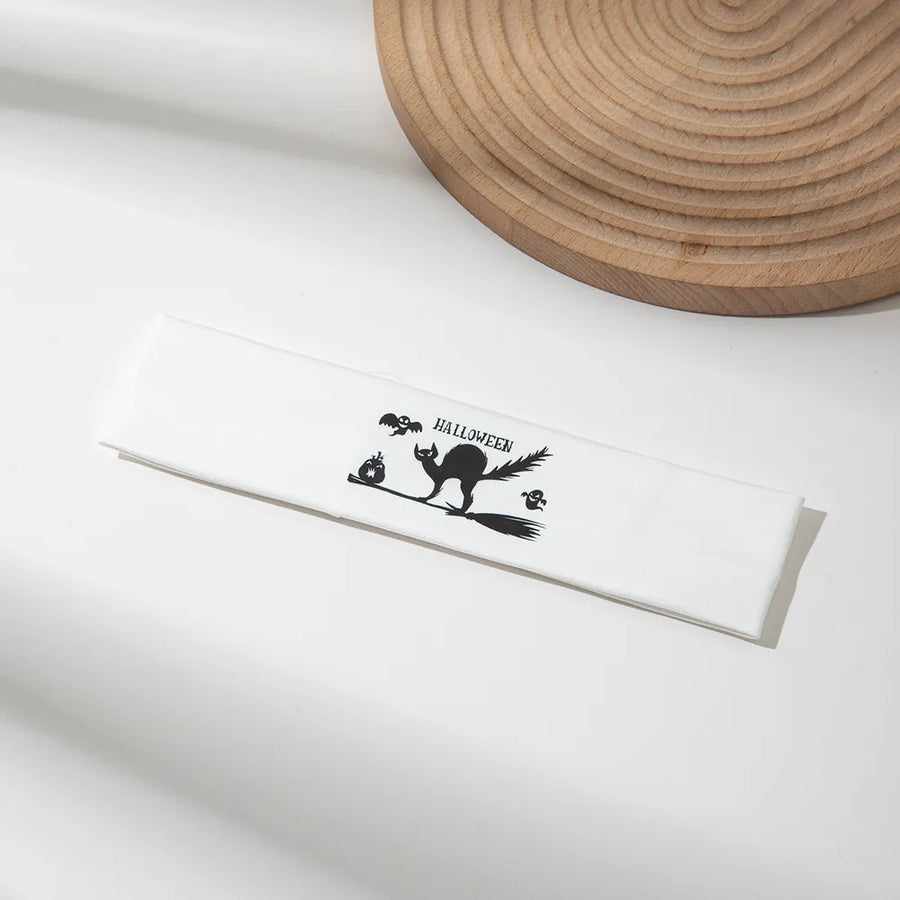 White headband with black Halloween graphic of a cat on a broomstick, pumpkins, bats and ghosts.
