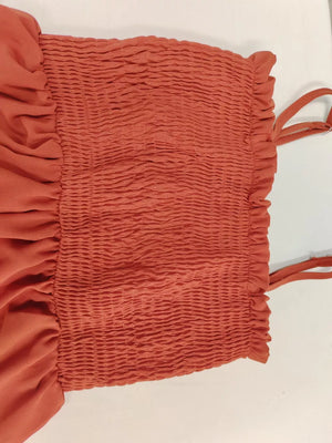 Orange-red smocked romper with ruffle trim and adjustable straps.