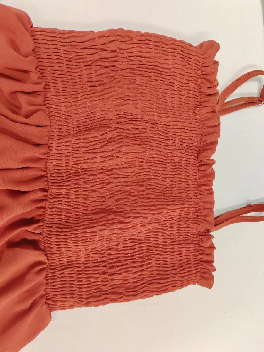 Orange-red smocked romper with ruffle trim and adjustable straps.