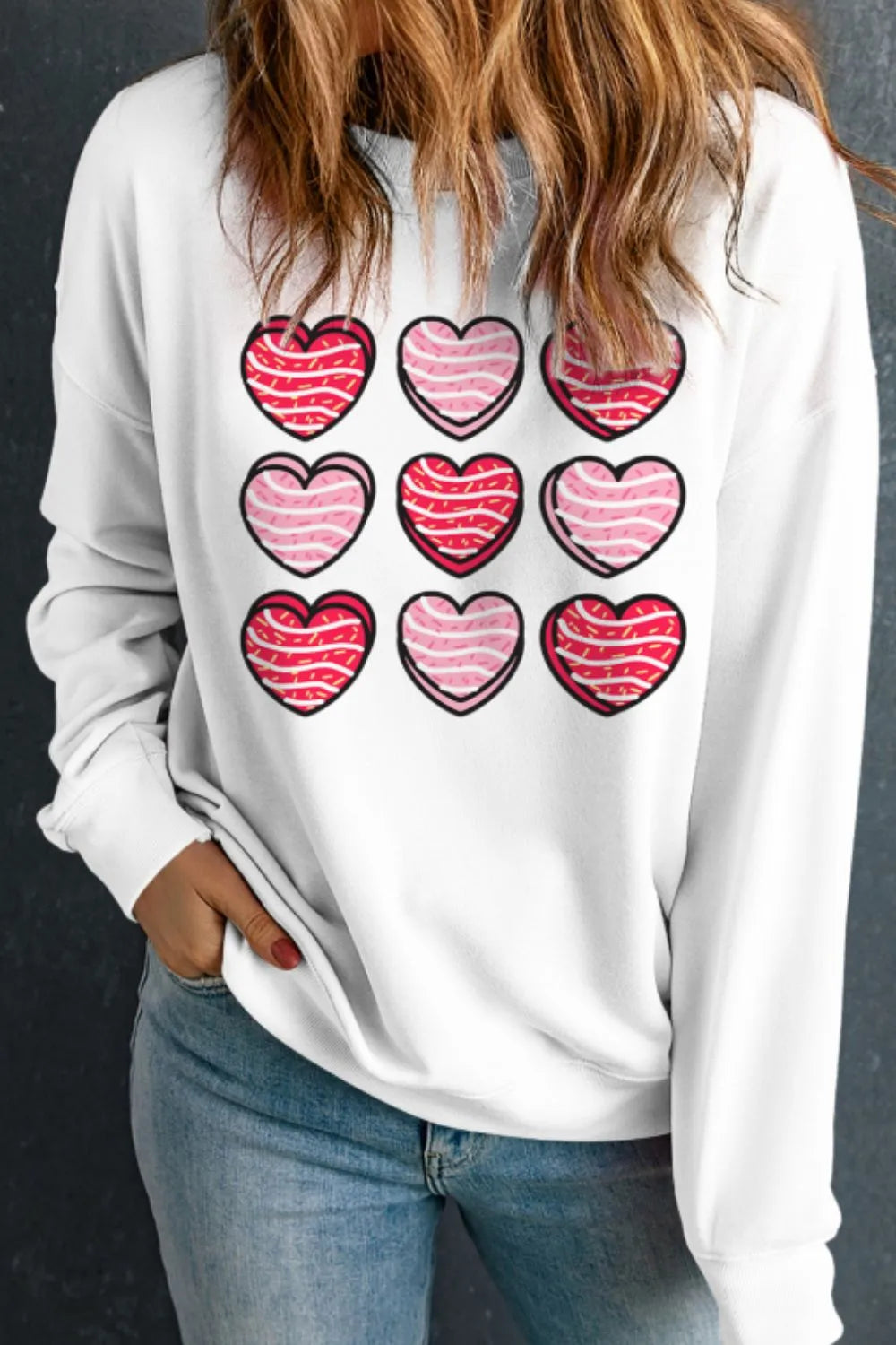 White crewneck sweatshirt with a grid of nine pink and red heart graphics.