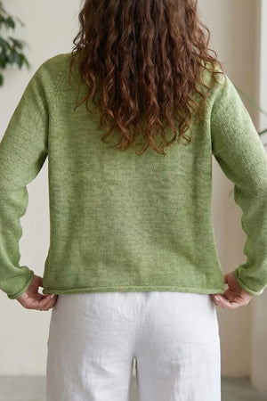 Green knit sweater with long sleeves and a crew neck, styled with white linen pants.