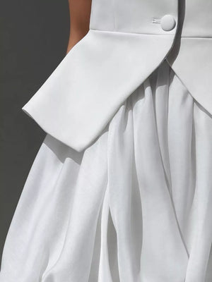 White structured blazer over a flowing white skirt with delicate pleats.