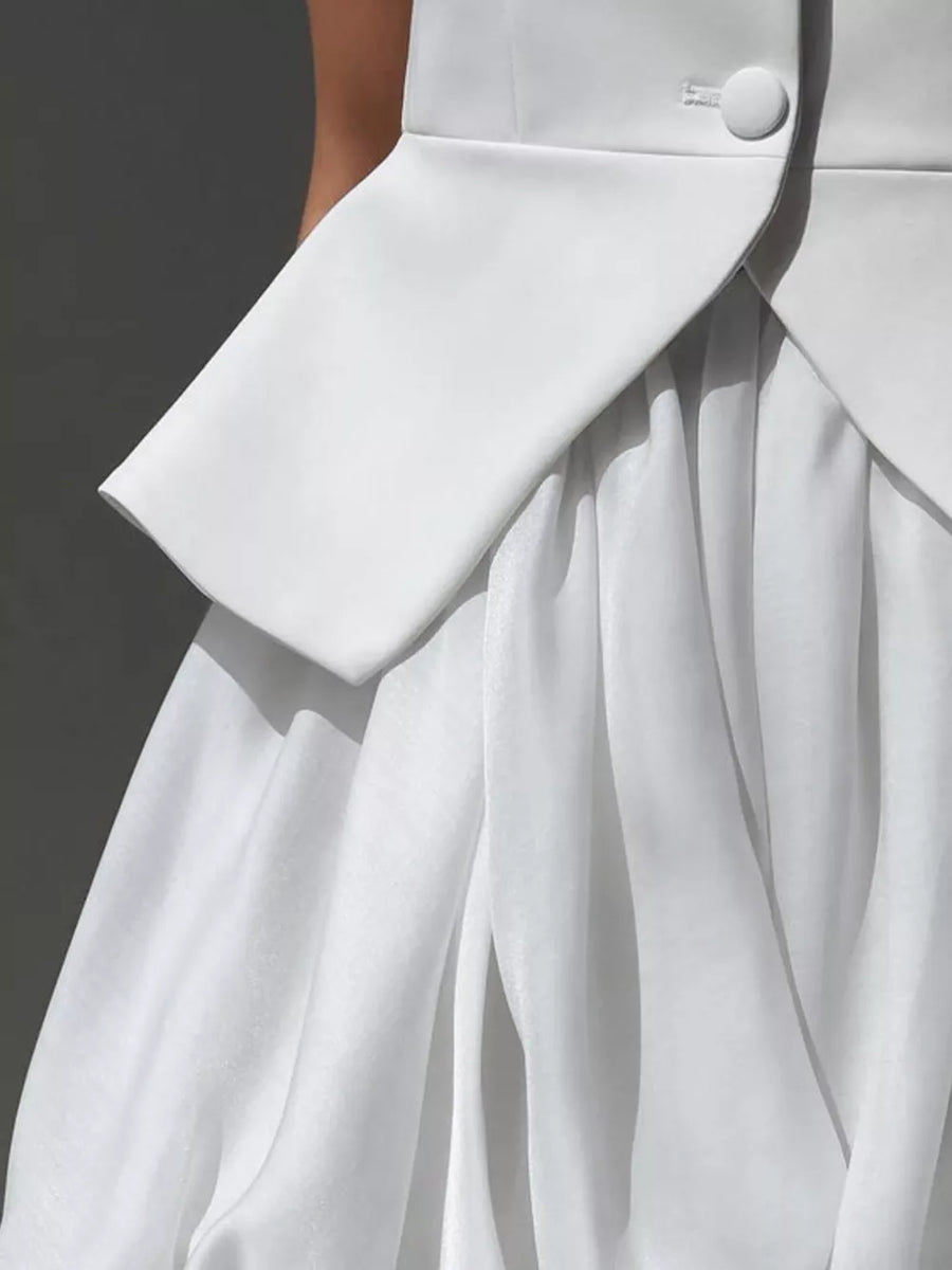 White structured blazer over a flowing white skirt with delicate pleats.