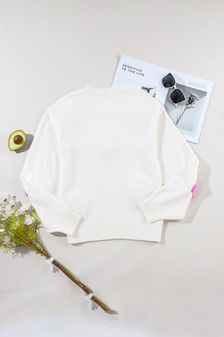 White knit sweater with embroidered pink blooms on the sleeves and a crew neckline.