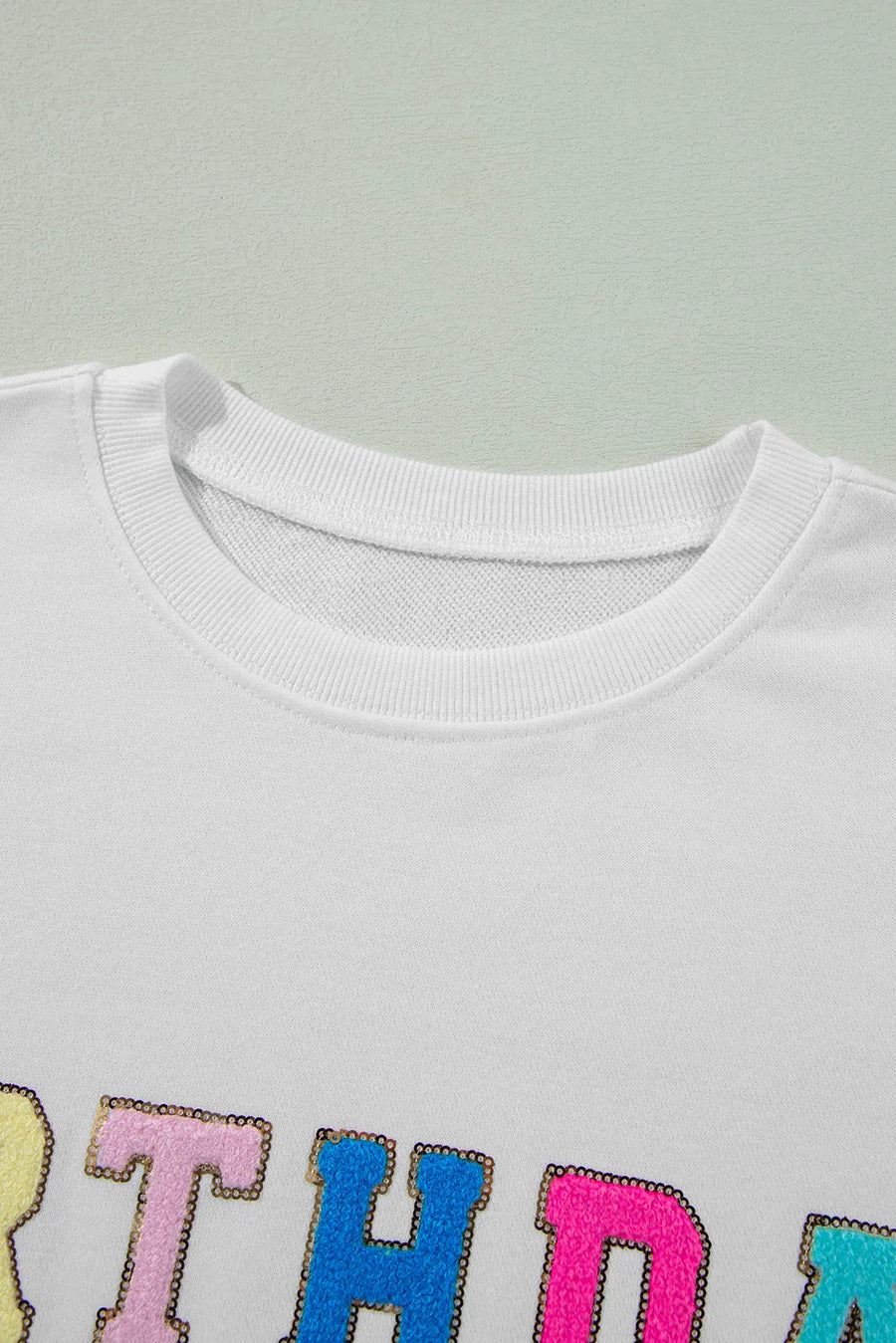White sweatshirt with colorful sequin trim letters spelling "BIRTHDAY QUEEN