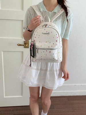 White mini backpack with colorful star pattern and front zipper pocket.