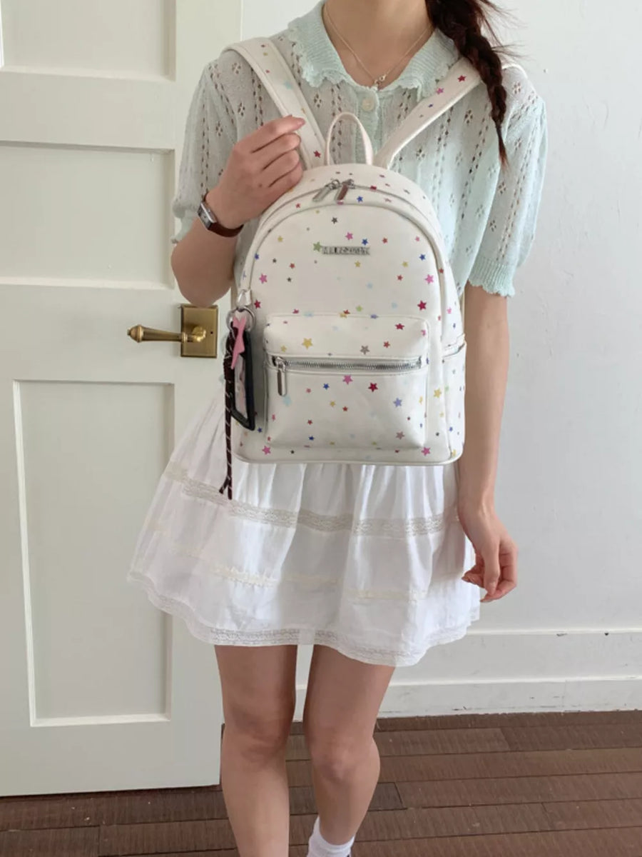 White mini backpack with colorful star pattern and front zipper pocket.