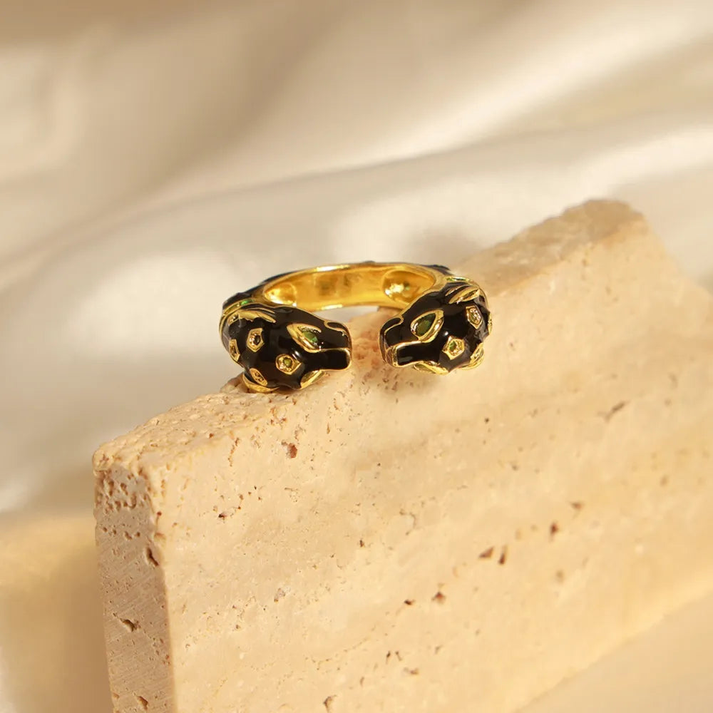 Gold open ring with black enamel panther heads and green gem eyes