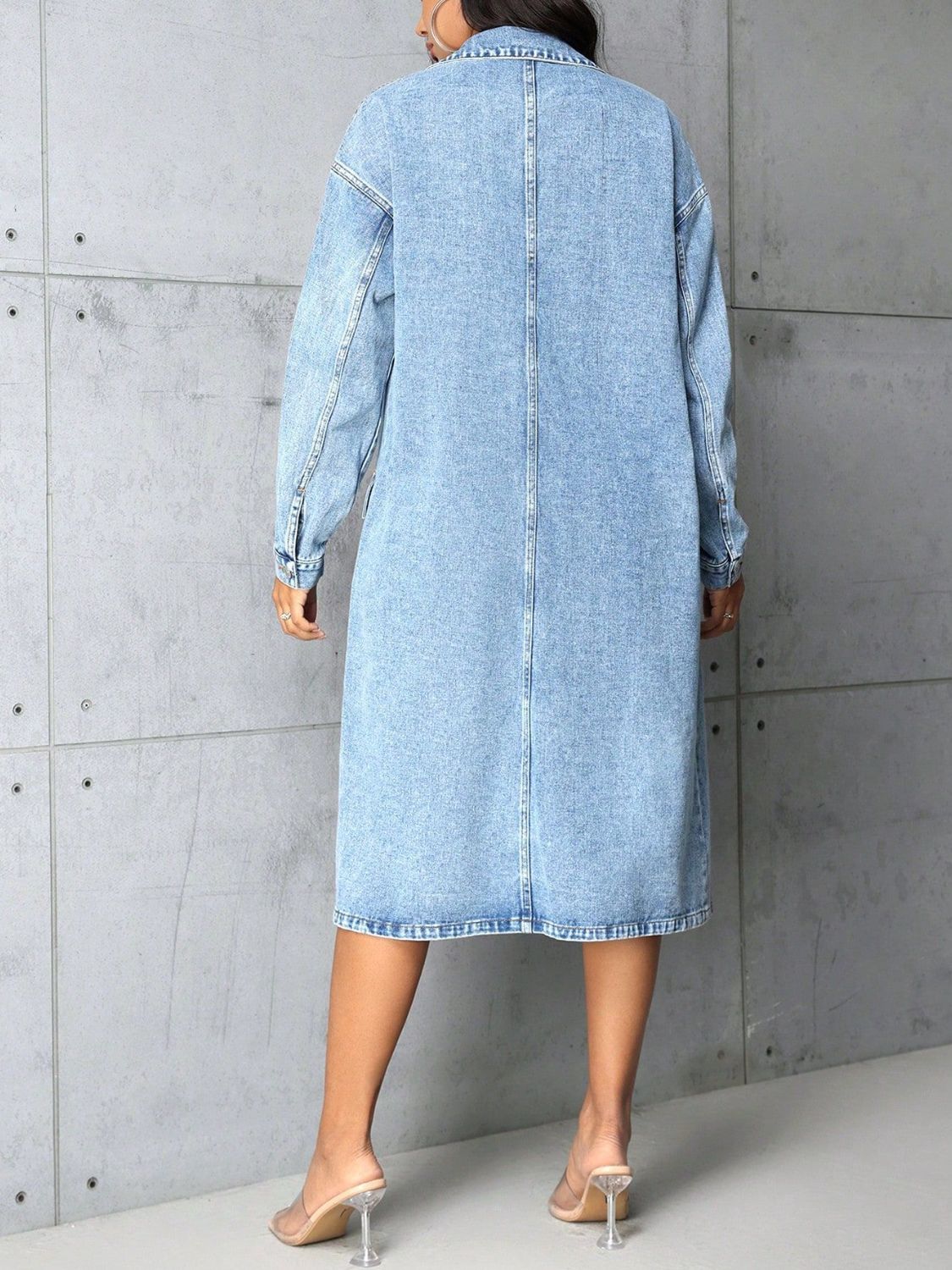 Medium wash denim duster coat with collared neckline, buttoned front, and long sleeves.