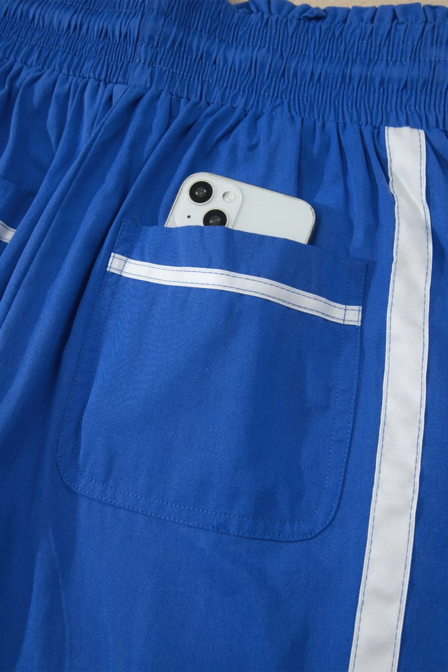 Blue smocked waist cropped casual pants with white stripe detail and pocket holding a phone.