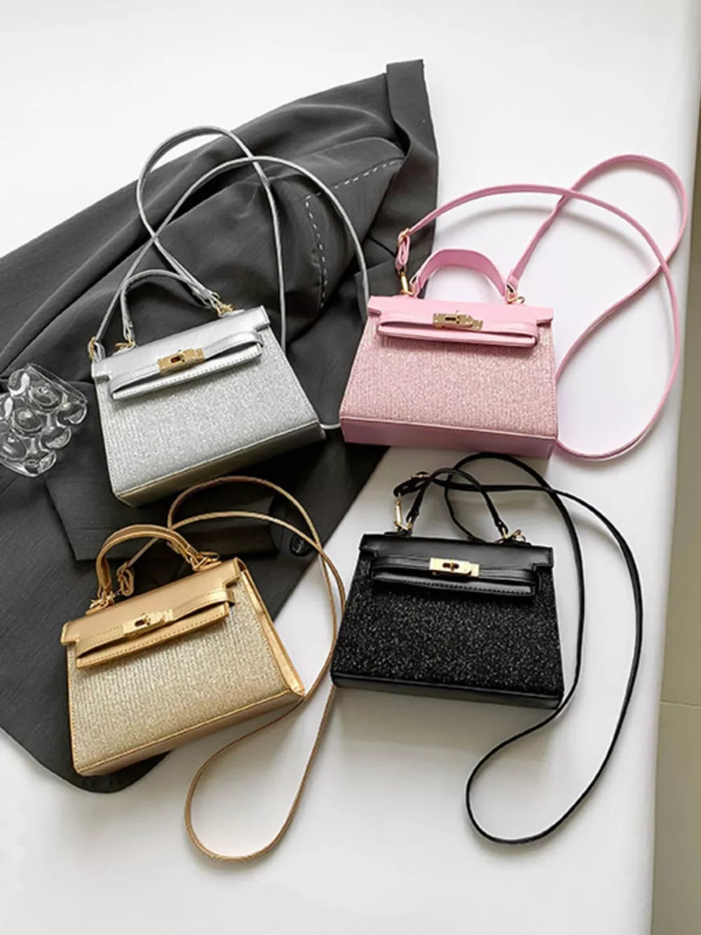 Glitter textured mini crossbody bags in gold, pink, silver, and black with top handles and shoulder straps.