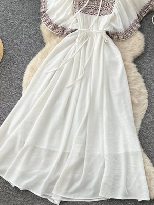 White embroidered V-neck maxi dress with tie waist and flowing skirt.
