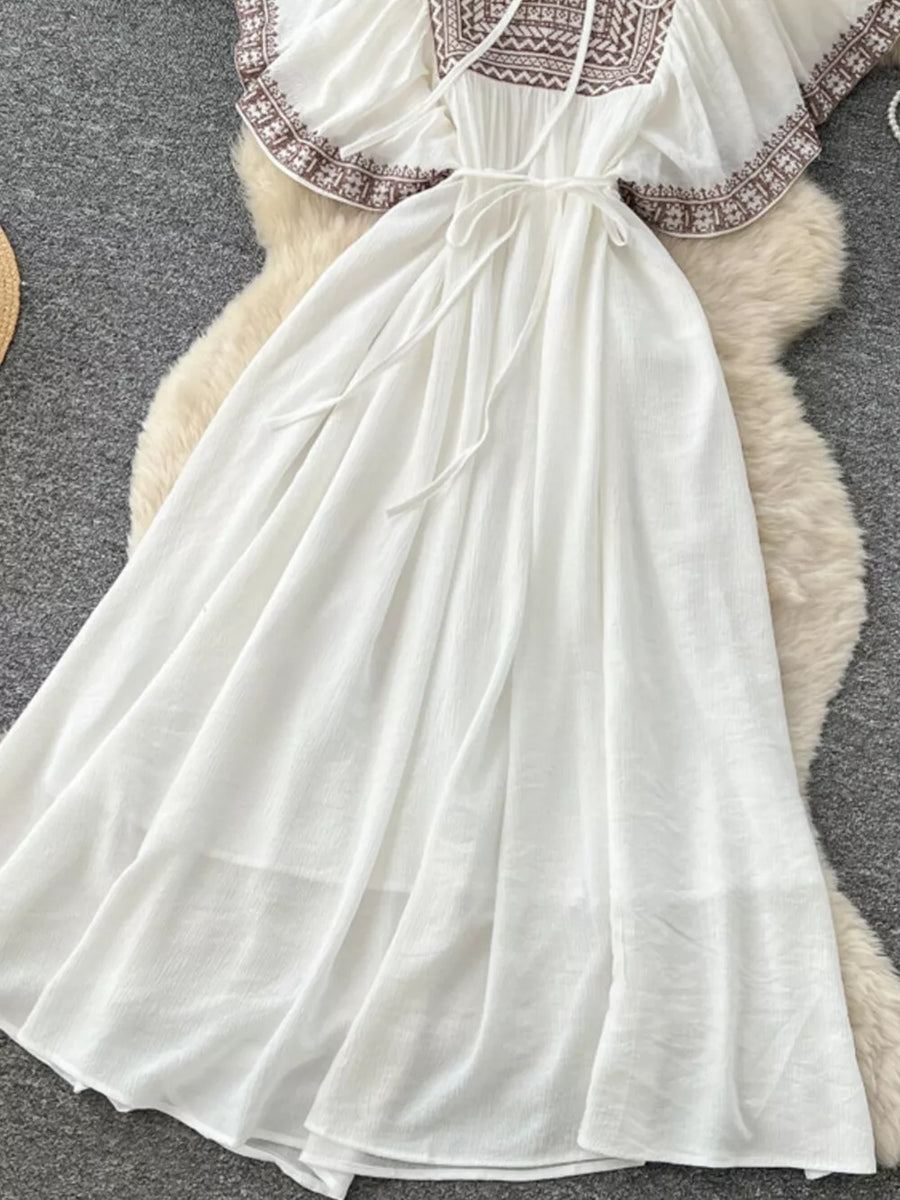 White embroidered V-neck maxi dress with tie waist and flowing skirt.