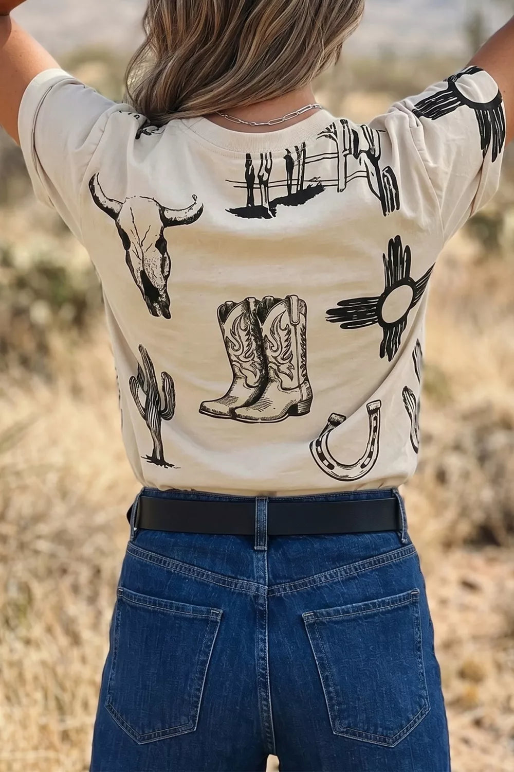 Cream crew neck t-shirt with western graphic print including cowboy boots, bull skull, cactus, and horseshoe.