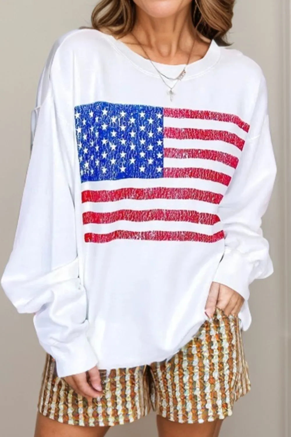 White crewneck sweatshirt with distressed American flag graphic and long sleeves.