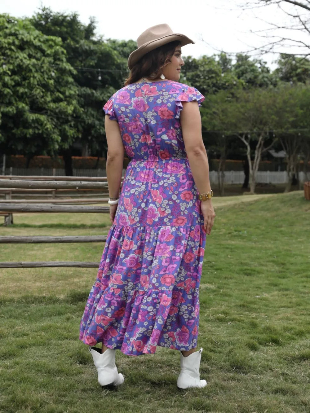 Vibrant floral tiered maxi dress with cap sleeves and cinched waist, styled with white boots and a hat.