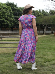 Vibrant floral tiered maxi dress with cap sleeves and cinched waist, styled with white boots and a hat.