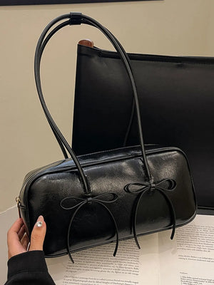 Black patent leather shoulder bag with bow details and thin straps.