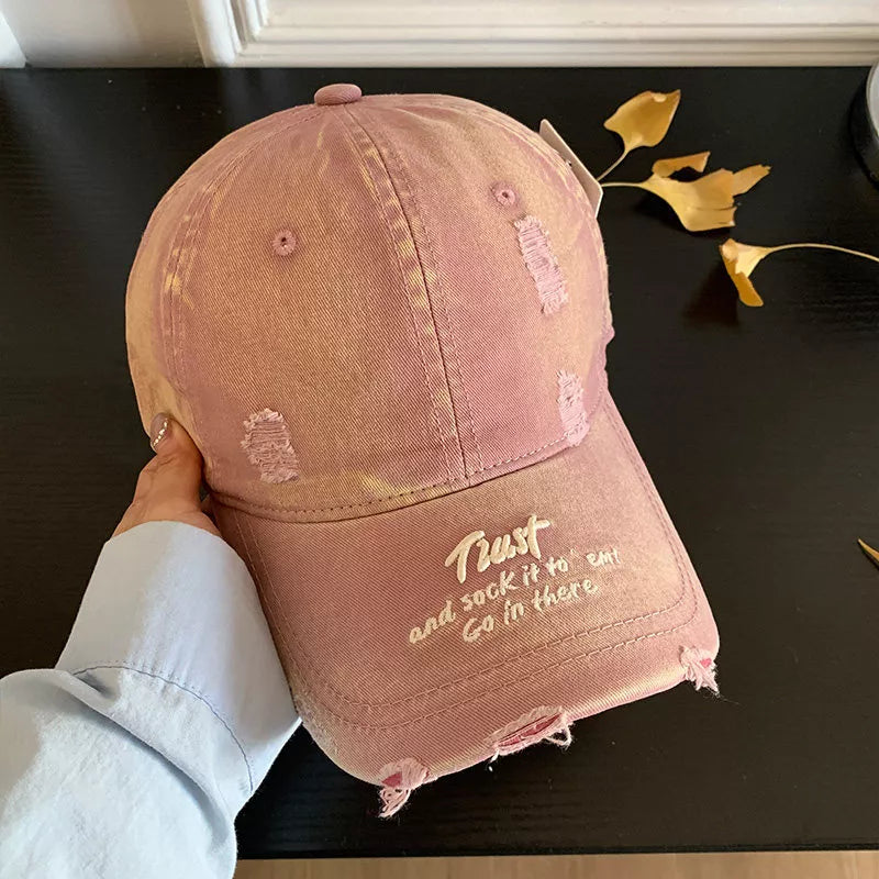 Distressed pink baseball cap with embroidered text and frayed details