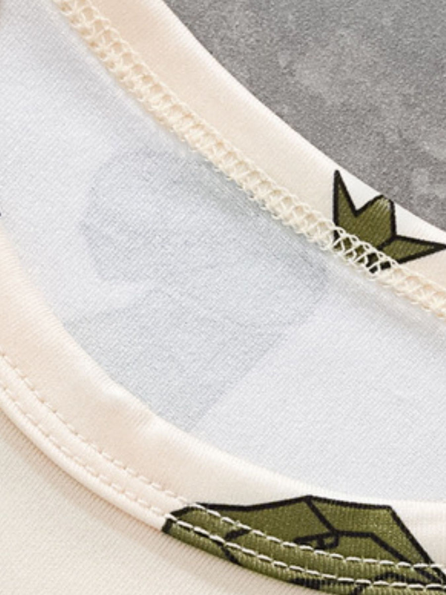Toddler tee with dinosaur print and cream trim, showing neckline detail.