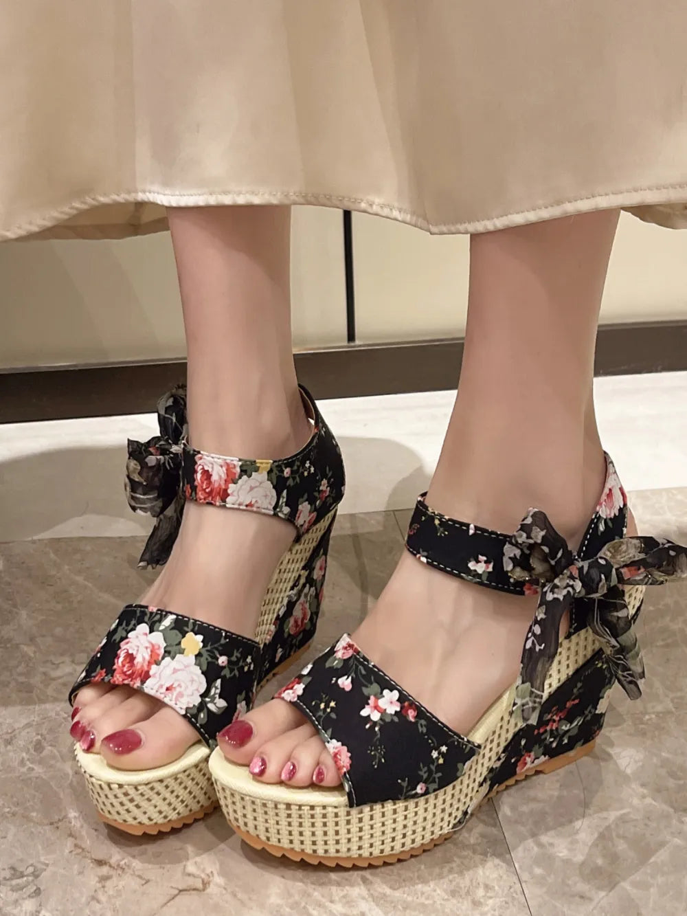 Black floral wedge sandals with ankle strap bows and woven wedge heel.