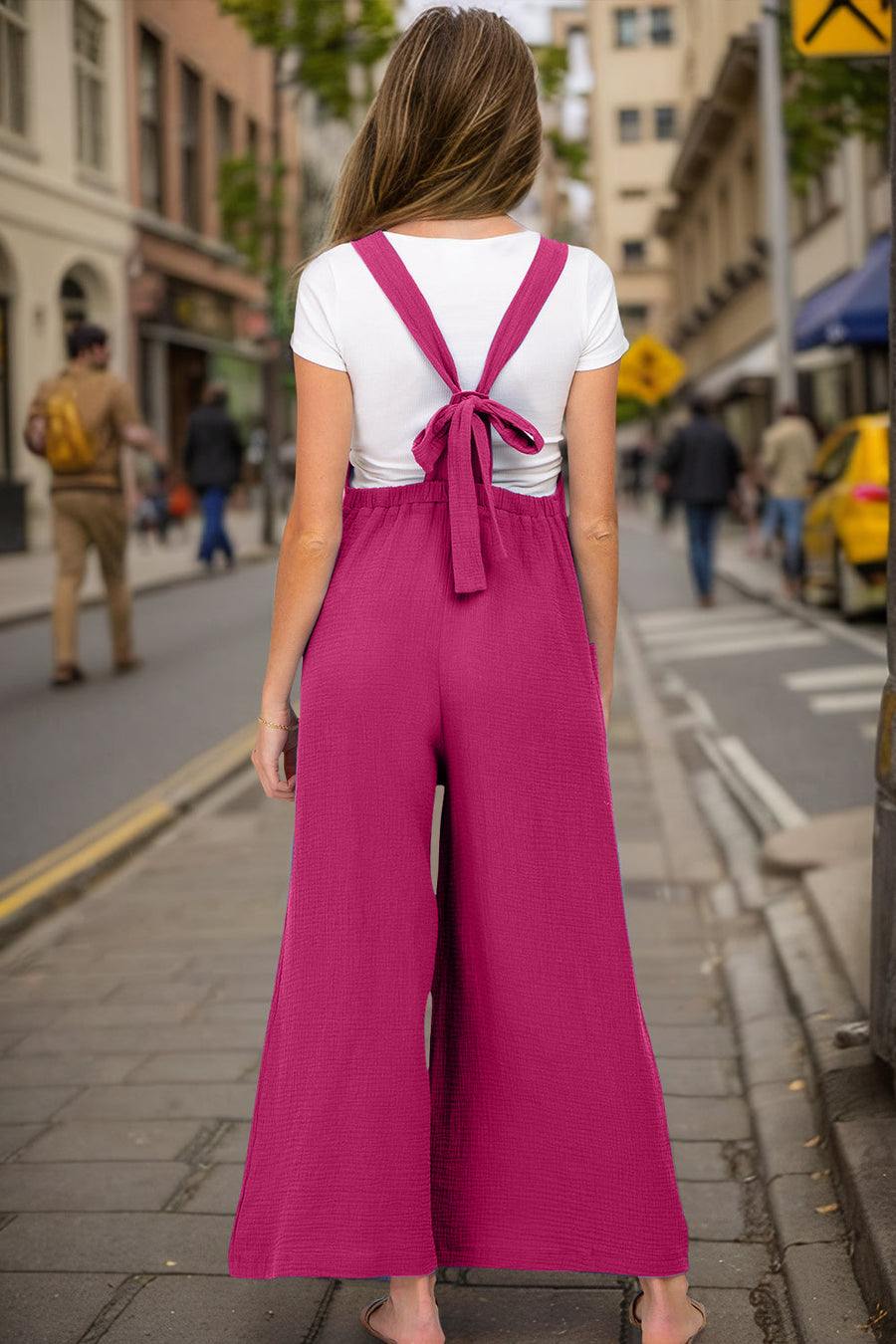 Gathered bib wide-leg jumpsuit in hot pink with tie-back straps and textured fabric.
