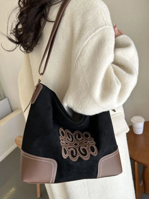 Black suede hobo bag with brown leather trim and appliqué detail, contrast stitching.