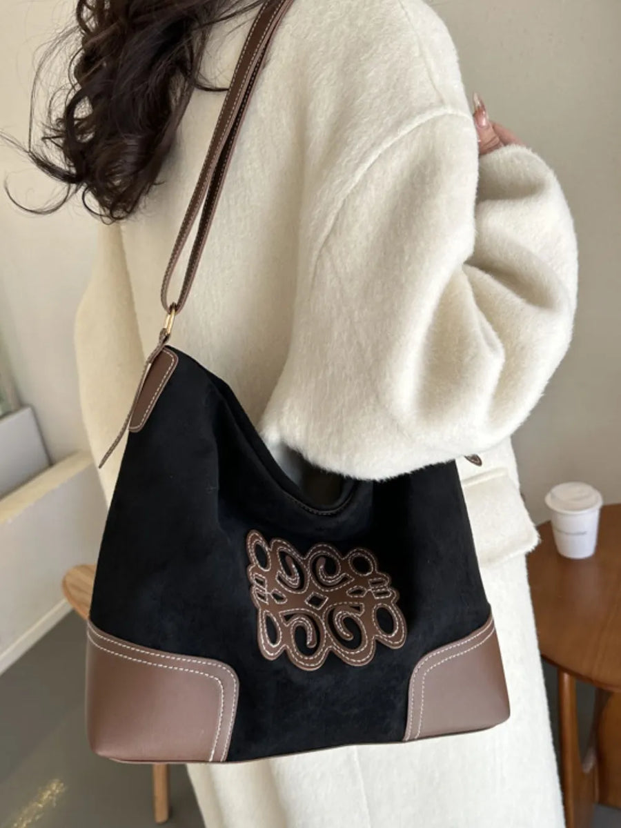 Black suede hobo bag with brown leather trim and appliqué detail, contrast stitching.