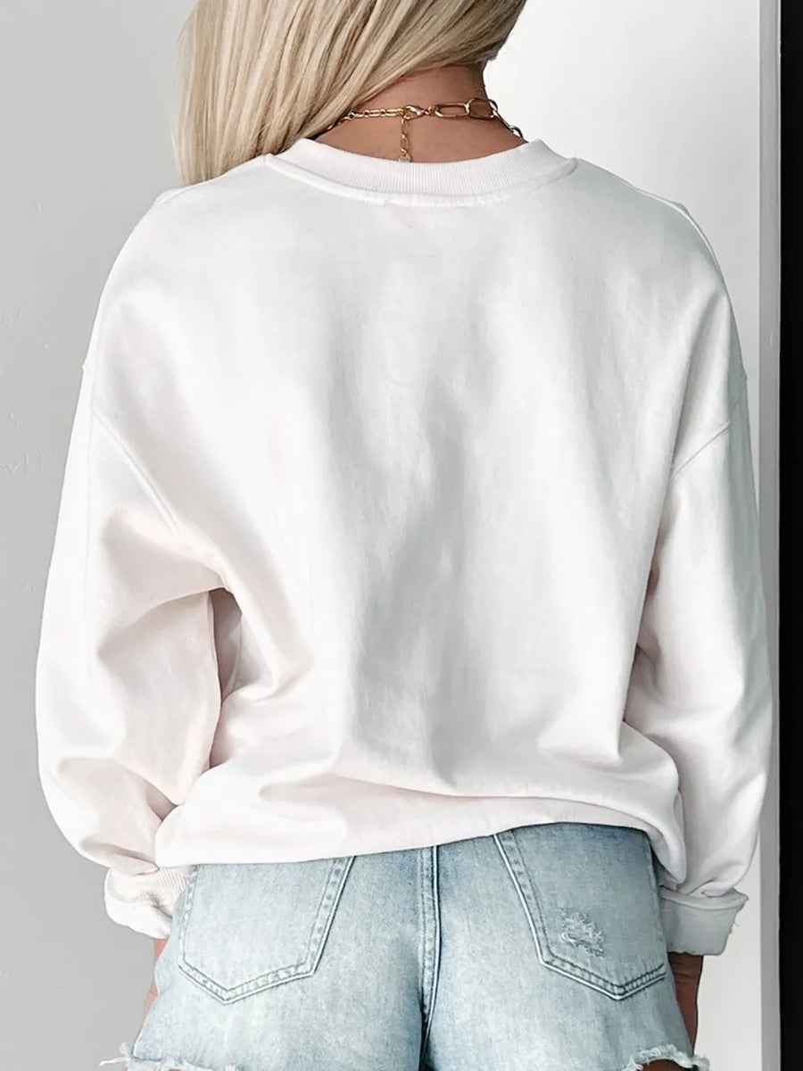 White crewneck sweatshirt with relaxed fit and cuffed sleeves, styled with denim shorts.