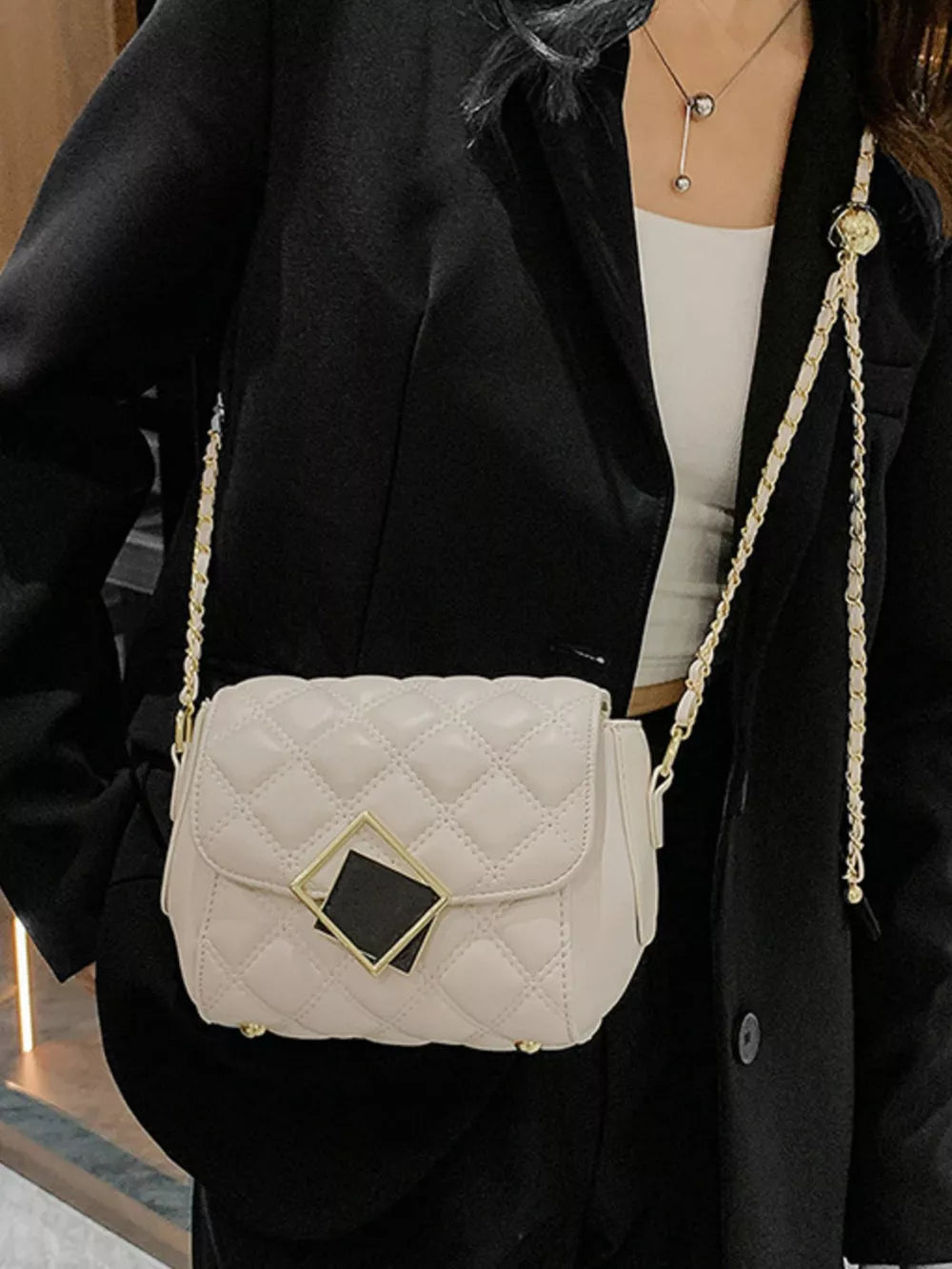 Elegant quilted crossbody bag in white with gold chain strap and geometric clasp detail.