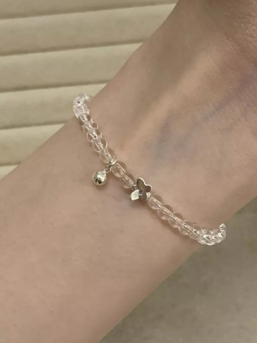 Crystal bead bracelet with silver butterfly charm and bell accent.