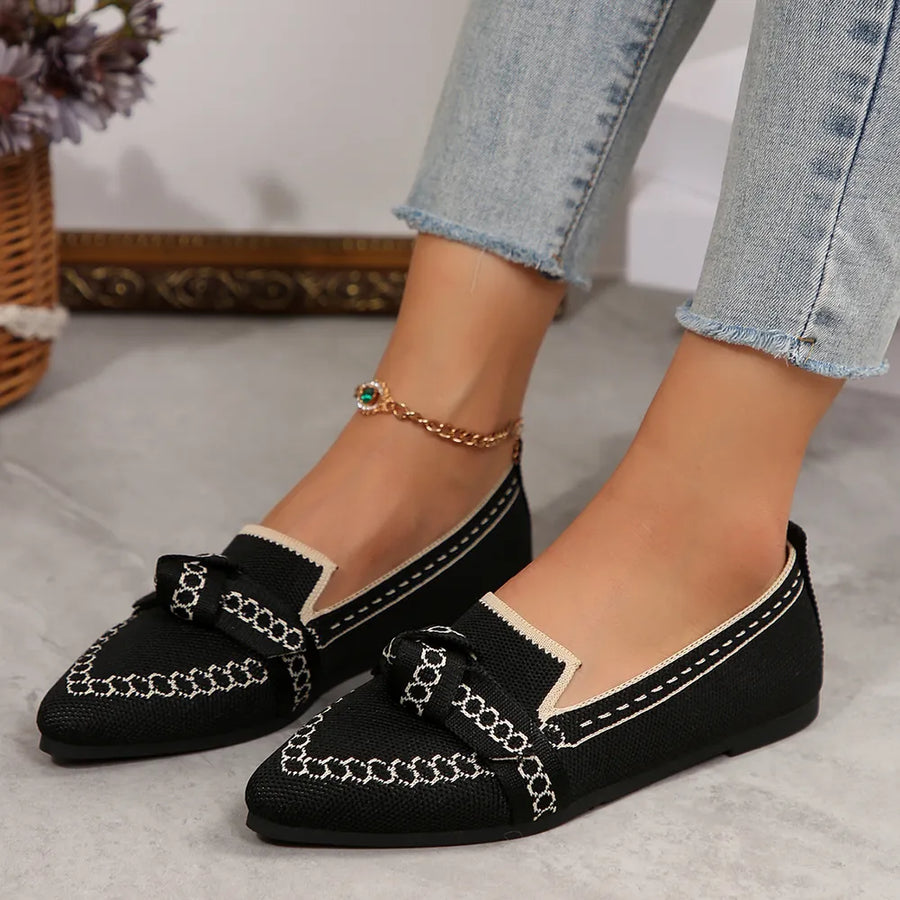 Black chain-stitched knit bow pointed flats with cream trim and white stitching.