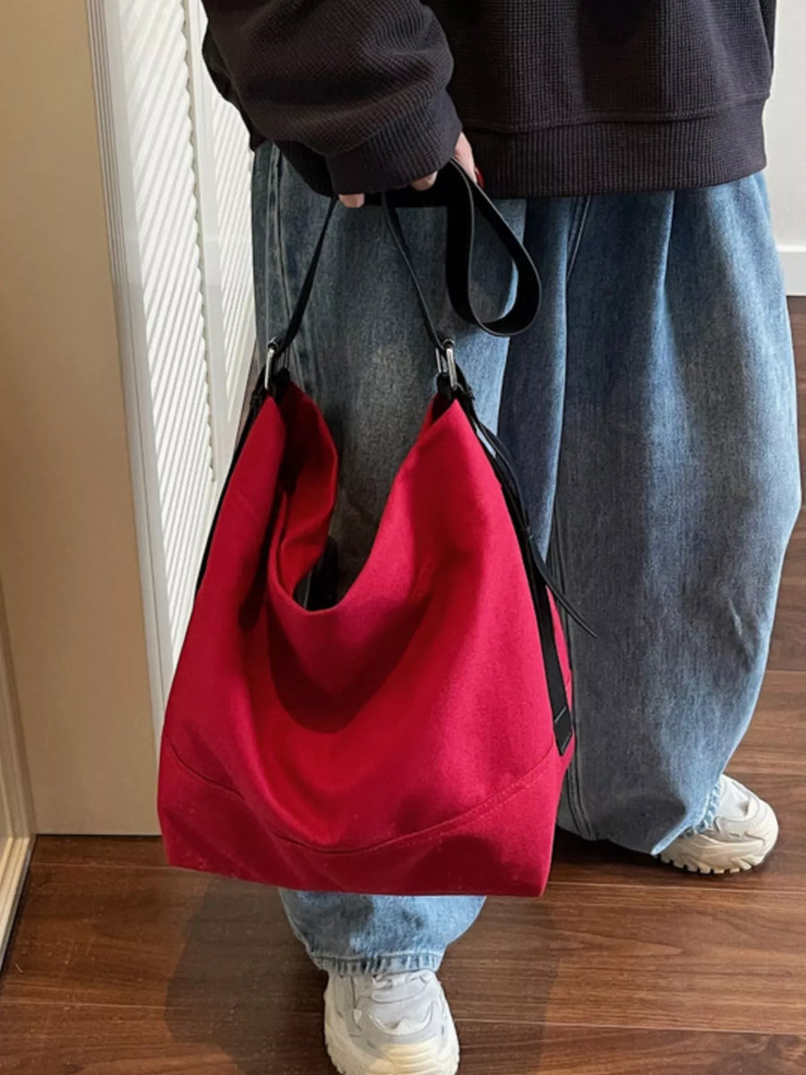 Red hobo bag with adjustable strap and black trim, styled casually with jeans.