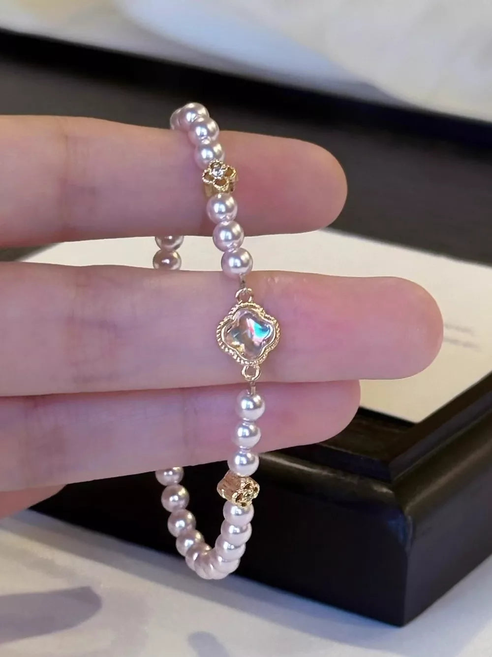 Delicate pearl bracelet with gold clover charm and iridescent center.