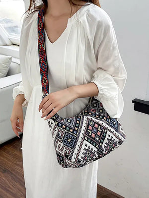 Embroidered geometric hobo bag with colorful strap, worn by a model in a white dress.