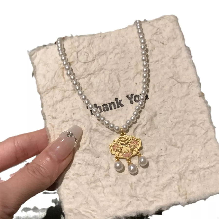 Gold lotus pendant necklace with pearl accents and chain, on textured paper.