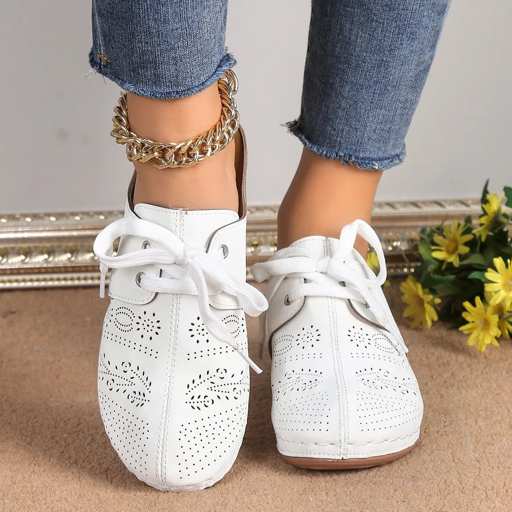 White perforated lace-up mule flats with floral cutouts and a gold chain anklet.