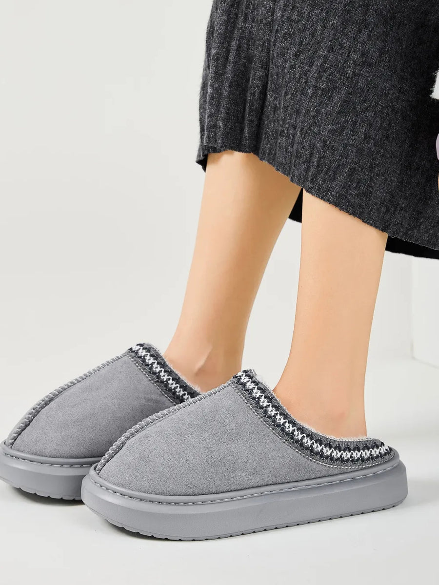 Gray shearling house slippers with embroidered trim and faux fur lining.