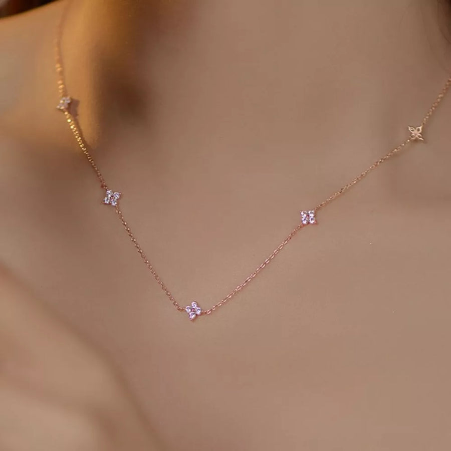 Delicate rose gold necklace with small clover charms and crystal accents.