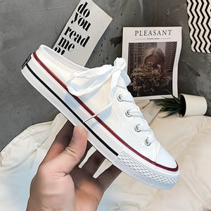White canvas mule sneakers with red and black contrast trim and white laces.