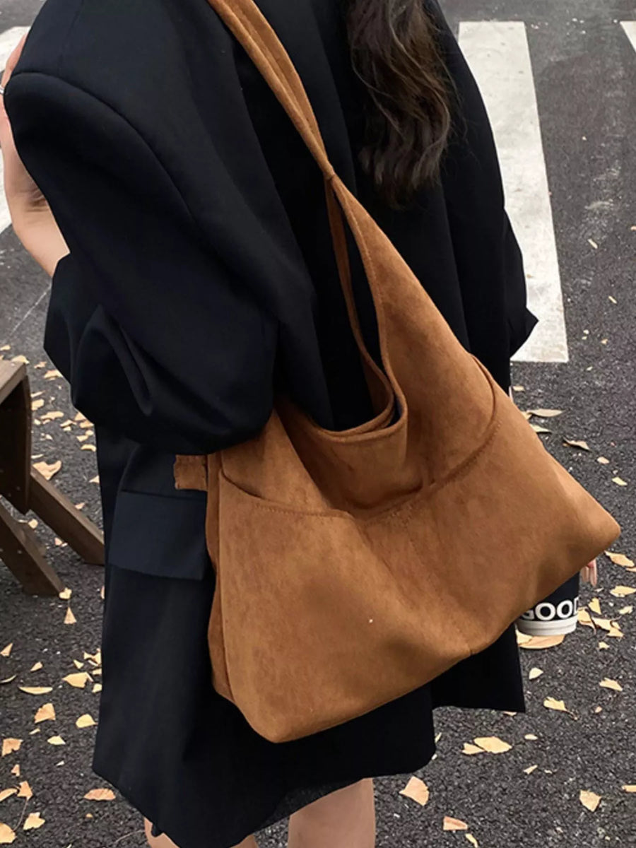 Large brown suede shoulder bag with exterior pockets, worn over a black blazer.