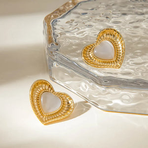 Golden heart stud earrings with ribbed details and a white cabochon center.