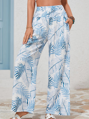 Tropical leaf print wide leg pants in white with blue palm leaves, featuring a smocked waistband and pockets.