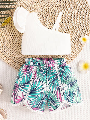 White asymmetrical top with ruffled sleeve and floral print shorts with pom-pom trim.