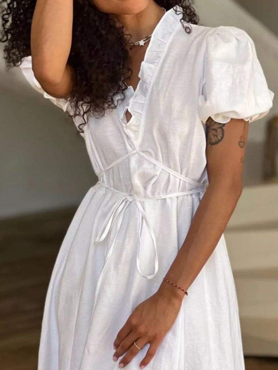 White linen dress with ruffled neckline, puff sleeves, and tie waist.